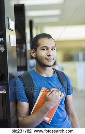 Stock Image - Portrait of Mixed Race boy holding book in library. Fotosearch