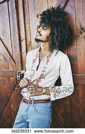 Stock Image - Portrait of Mixed Race man leaning on barn door. Fotosearch
