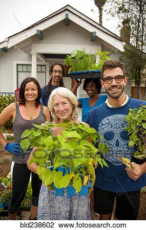 Stock Image - Portrait of neighbors holding plants near house. Fotosearch