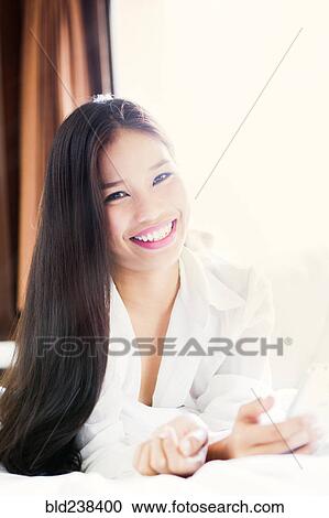 Portrait of smiling Asian teenage girl laying on bed View Large Photo Image Stock Image - Portrait of smiling Asian teenage girl laying on bed. Fotosearch