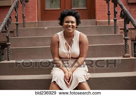 Stock Photo - Portrait of smiling Black woman sitting on urban front stoop. Fotosearch
