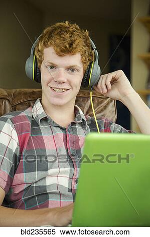 Stock Photography - Portrait of smiling Caucasian boy listening to laptop with headphones. Fotosearch