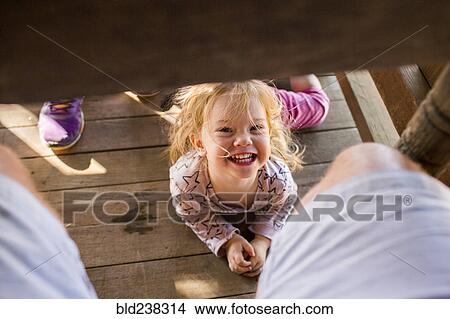 Picture - Portrait of smiling Caucasian girl laying underneath table. Fotosearch