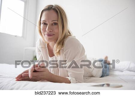 Stock Image - Portrait of smiling Caucasian woman laying on bed. Fotosearch