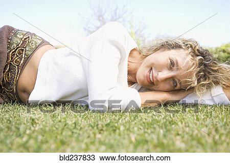 Stock Image - Portrait of smiling Caucasian woman laying in grass. Fotosearch