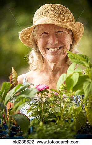 Stock Image - Portrait of smiling Caucasian woman holding tray of flowers. Fotosearch