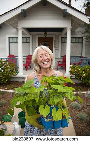Portrait of smiling Caucasian woman holding tray of plants near house View Large Photo Image Stock Photo - Portrait of smiling Caucasian woman holding tray of plants near house. Fotosearch