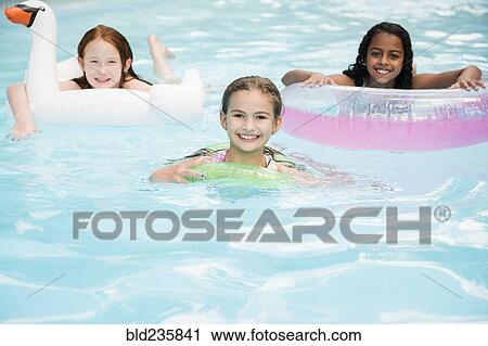 Stock Image - Portrait of smiling girls floating in swimming pool. Fotosearch