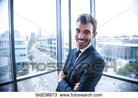 Stock Image - Portrait of smiling Hispanic businessman posing near window. Fotosearch