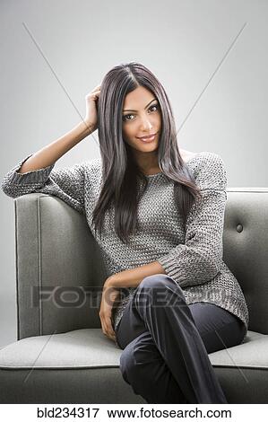 Stock Photo - Portrait of smiling Indian woman sitting on sofa. Fotosearch