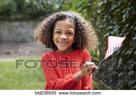 Stock Image - Portrait of smiling Mixed Race girl waving little American flag. Fotosearch