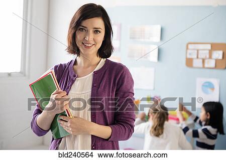Portrait of smiling teacher holding notebooks in classroom View Large Photo Image Picture - Portrait of smiling teacher holding notebooks in classroom. Fotosearch