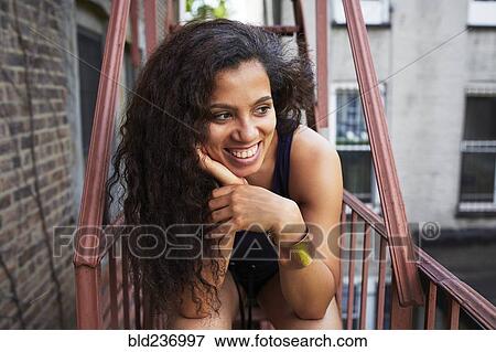 Stock Photo - Portrait of smiling woman relaxing on urban fire escape. Fotosearch