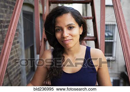 Stock Photography - Portrait of smiling woman sitting on urban fire escape. Fotosearch