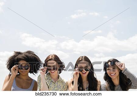 Portrait of smiling women holding sunglasses outdoors View Large Photo Image Stock Image - Portrait of smiling women holding sunglasses outdoors. Fotosearch