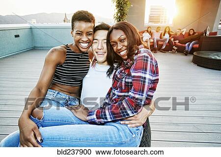 Stock Image - Portrait of smiling women on lap of man on rooftop. Fotosearch