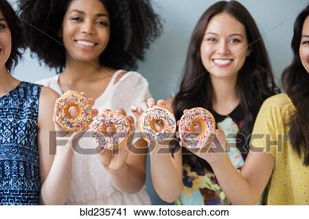 Stock Image - Portrait of smiling women posing with donuts. Fotosearch