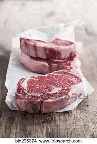 Picture - Raw rib eye steaks on butcher paper. Fotosearch