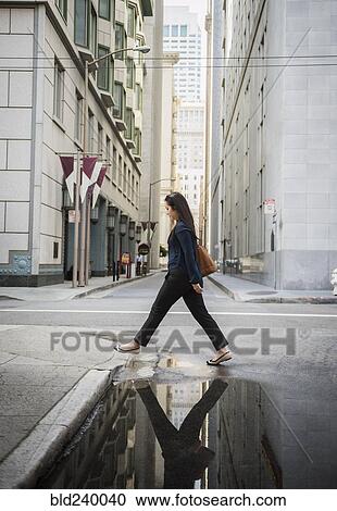 Stock Image - Reflection in puddle of Chinese businesswoman crossing street. Fotosearch