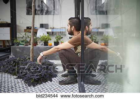 Picture - Reflection of sitting Hispanic man in atrium window . Fotosearch