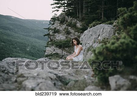 Stock Photo - Sad Caucasian woman sitting on mountain. Fotosearch