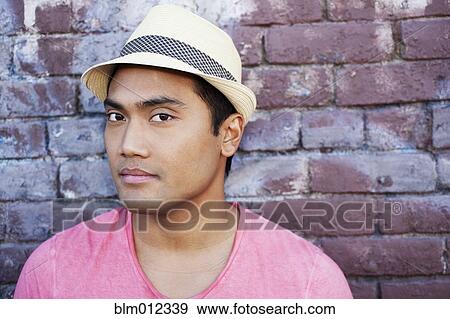 Stock Photo - Serious Asian man near brick wall. Fotosearch