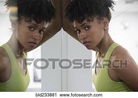 Stock Image - Serious Black woman leaning on mirror wall. Fotosearch