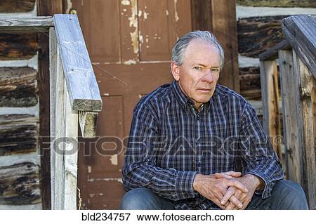 Stock Photo - Serious Caucasian man sitting on wooden front stoop. Fotosearch