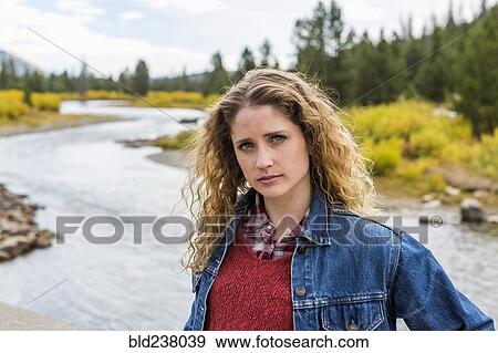 Stock Photo - Serious Caucasian woman standing near winding river. Fotosearch
