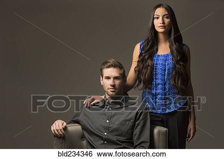Serious couple posing with armchair View Large Photo Image Stock Photograph - Serious couple posing with armchair. Fotosearch