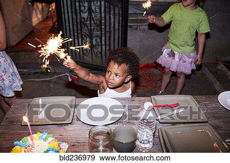 Stock Photo - Serious girl holding burning sparkler at backyard party. Fotosearch