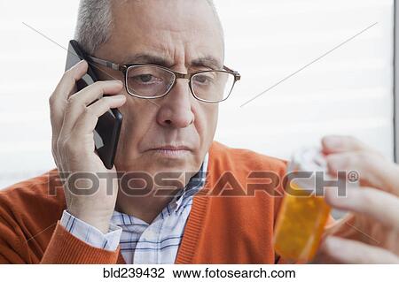 Serious Hispanic man talking on cell phone holding prescription bottle View Large Photo Image Stock Image - Serious Hispanic man talking on cell phone holding prescription bottle. Fotosearch