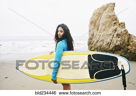 Serious Mixed Race woman carrying surfboard at beach View Large Photo Image Stock Photograph - Serious Mixed Race woman carrying surfboard at beach. Fotosearch