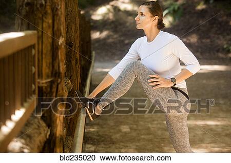 Stock Image - Serious woman stretching leg on forest path. Fotosearch