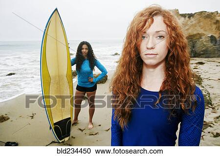 Stock Image - Serious women holding surfboards at beach. Fotosearch