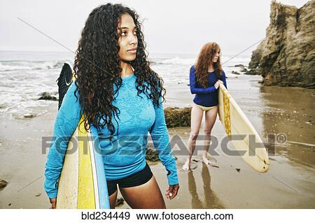 Stock Photo - Serious women holding surfboards at beach. Fotosearch
