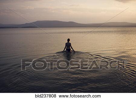 Stock Photo - Silhouette of Caucasian woman wading in lake. Fotosearch