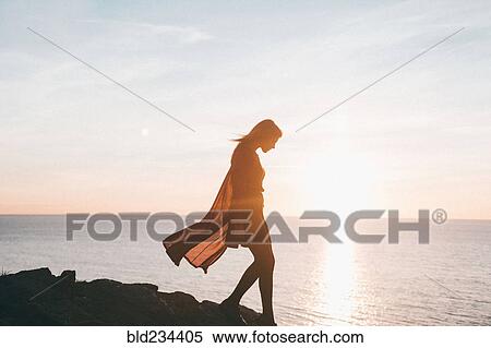 Stock Photography - Silhouette of Caucasian woman walking on rocks at ocean. Fotosearch