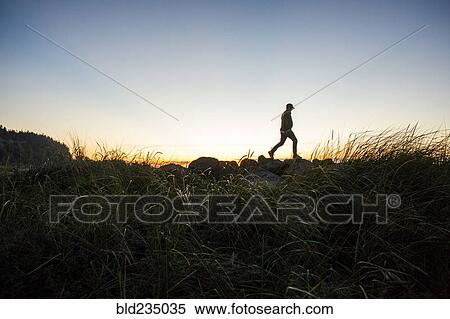 Silhouette of distant Caucasian man walking on rocks at sunset View Large Photo Image Stock Photography - Silhouette of distant Caucasian man walking on rocks at sunset. Fotosearch