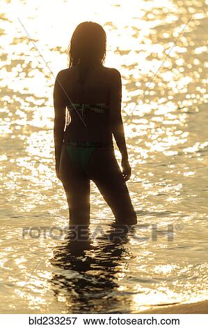 Stock Photo - Silhouette of Mixed Race woman wading in ocean at sunset. Fotosearch