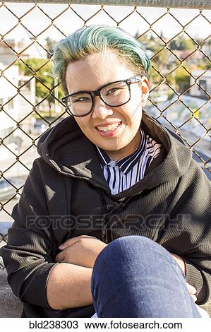 Smiling androgynous Asian woman leaning on chain-link fence View Large Photo Image Stock Image - Smiling androgynous Asian woman leaning on chain-link fence. Fotosearch