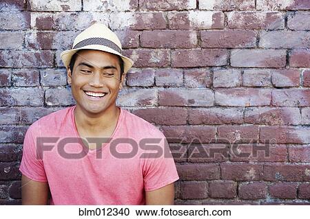 Stock Image - Smiling Asian man near brick wall. Fotosearch