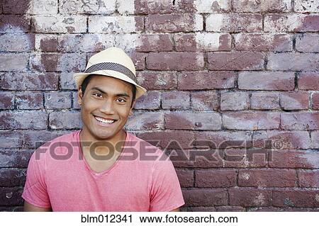 Stock Image - Smiling Asian man near brick wall. Fotosearch