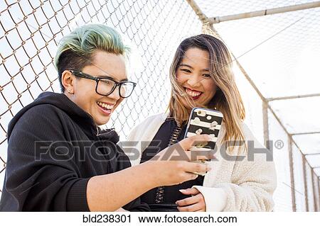 Stock Image - Smiling Asian women posing for cell phone selfie. Fotosearch