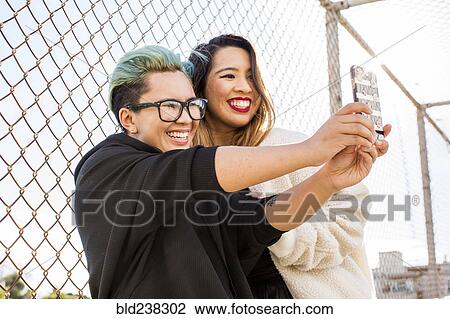 Stock Image - Smiling Asian women posing for cell phone selfie. Fotosearch