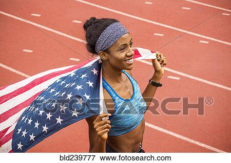 Smiling Black athlete holding American flag on track View Large Photo Image Stock Photo - Smiling Black athlete holding American flag on track. Fotosearch
