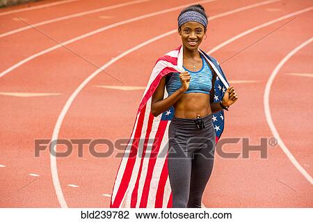 Stock Image - Smiling Black athlete posing with American flag on track. Fotosearch