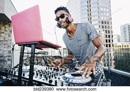 Stock Image - Smiling Black DJ on urban rooftop. Fotosearch