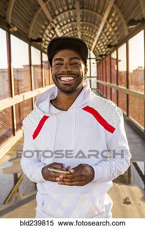 Smiling Black man holding cell phone on footbridge View Large Photo Image Stock Photography - Smiling Black man holding cell phone on footbridge. Fotosearch