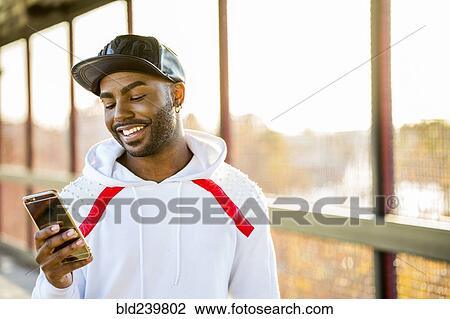 Stock Image - Smiling Black man texting on cell phone. Fotosearch